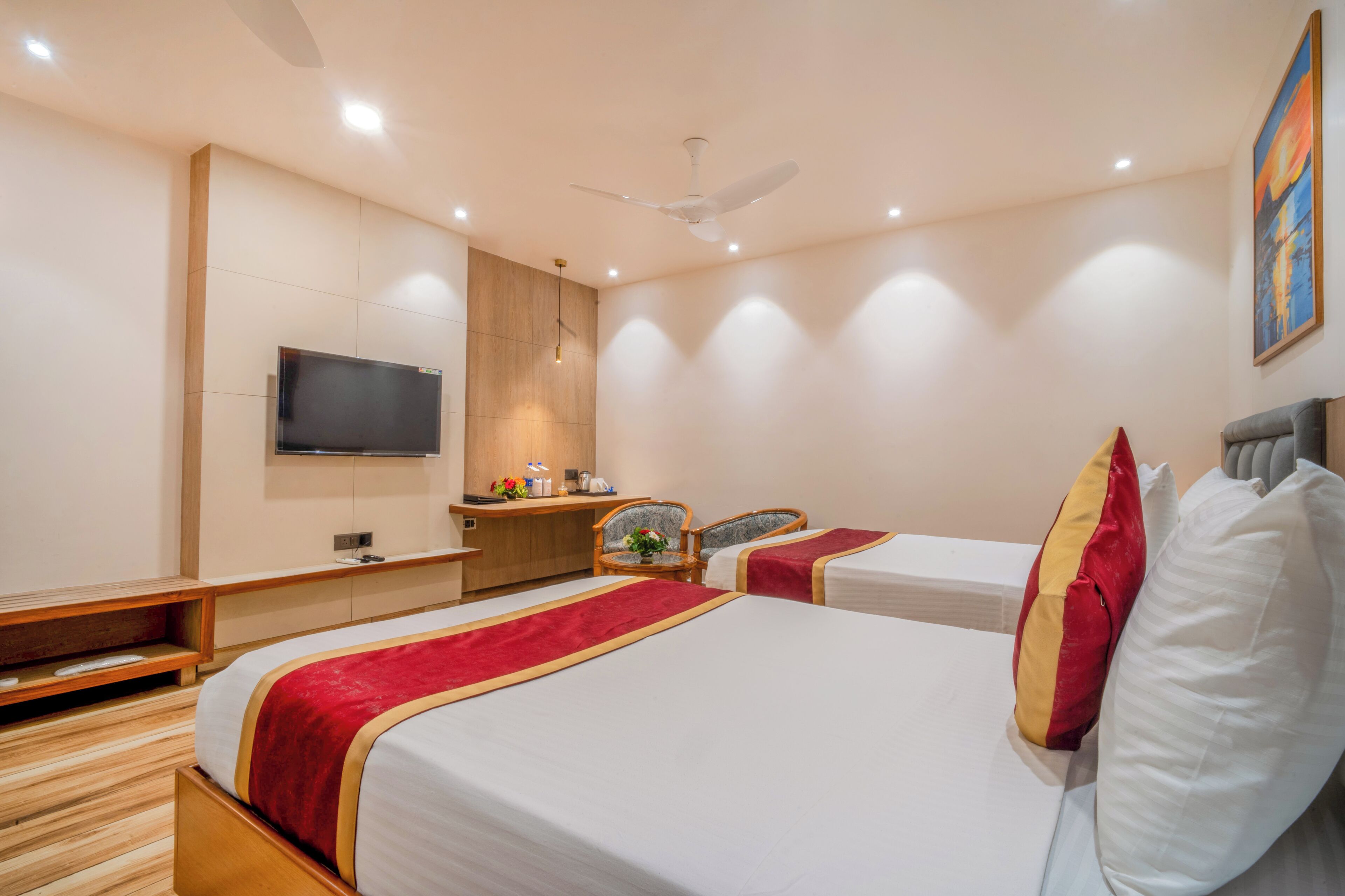A hotel room with two beds, a desk, a chair, a television, and a ceiling fan.