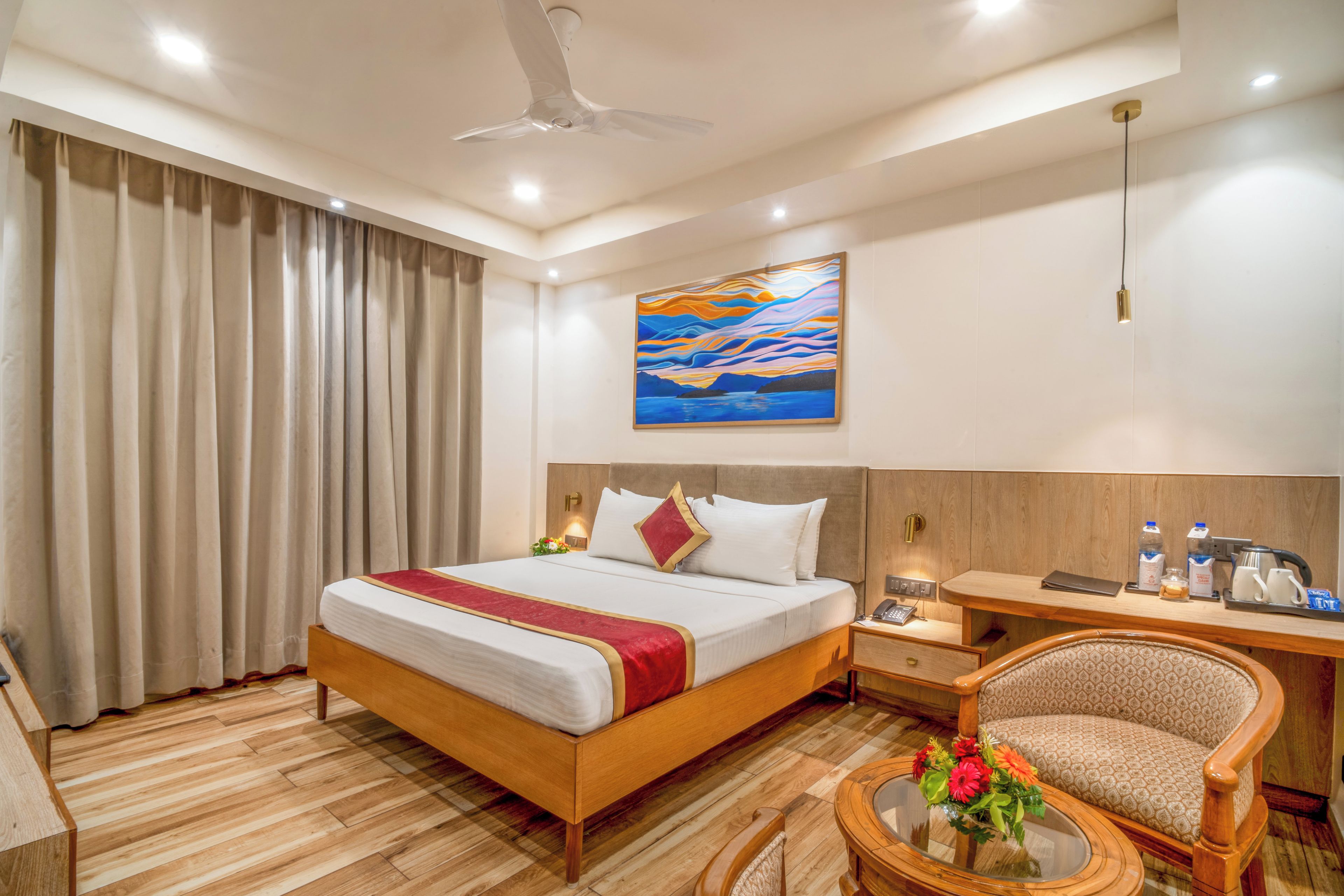 A hotel room with a wooden bed, a desk with a chair, a coffee maker, and a painting on the wall.