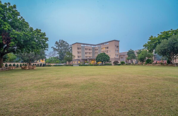 A large building with multiple floors, surrounded by a grassy area and trees. - HOTEL TATHAGAT ASHOK (Rajgir)