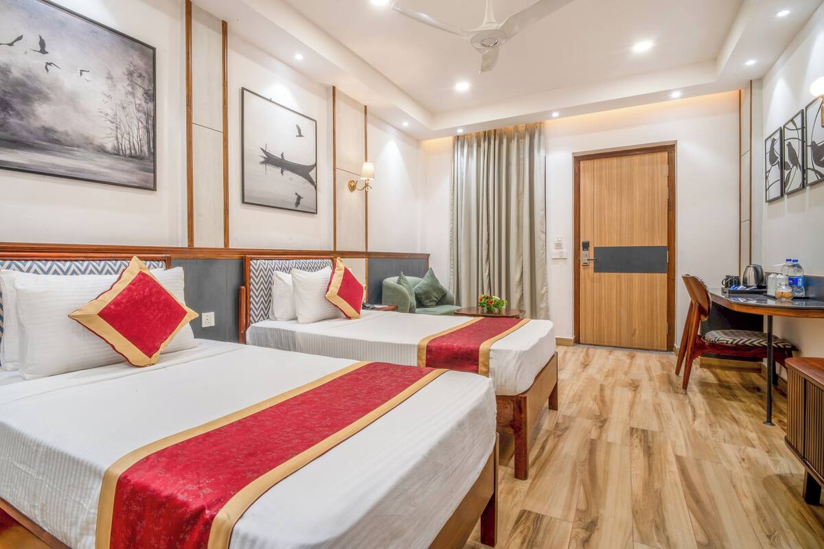 A hotel room with two beds, a wooden door, a desk with a chair, and artwork on the walls.
