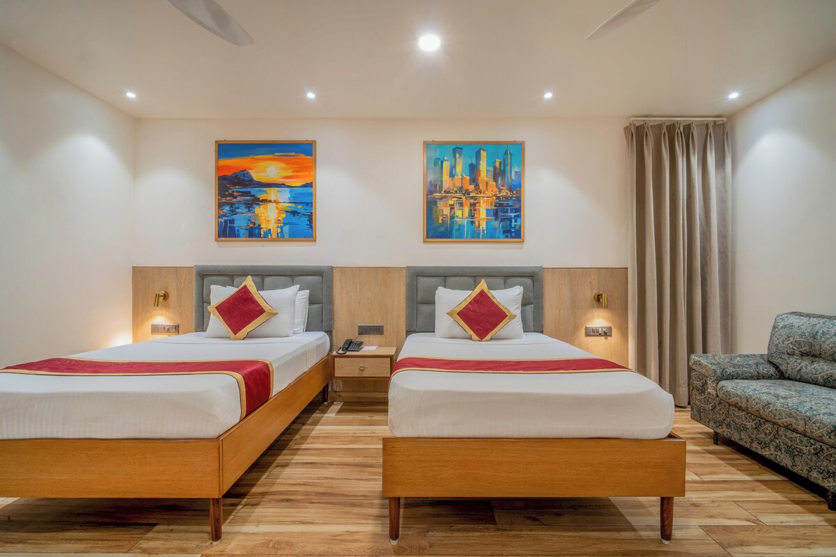 A hotel room with two beds, wooden flooring, and artwork on the walls.