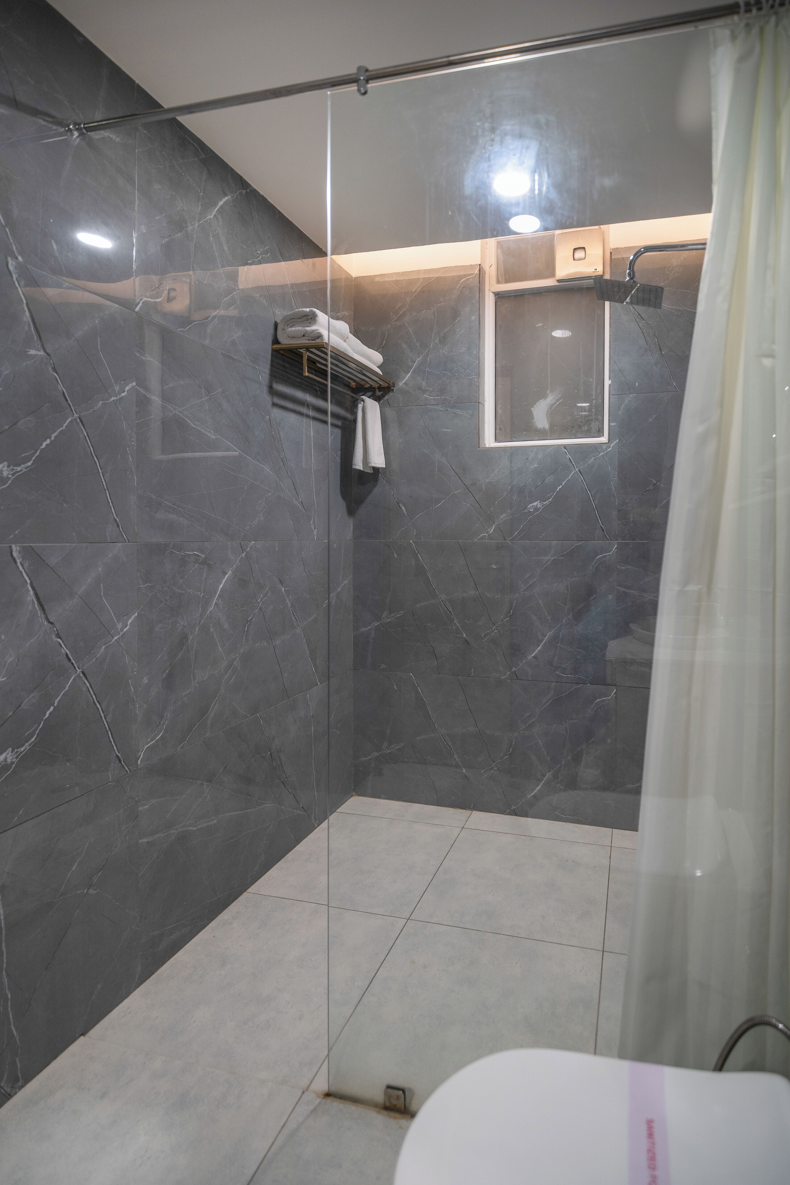 A modern shower area with dark marble walls, a glass door, and a white towel rack.