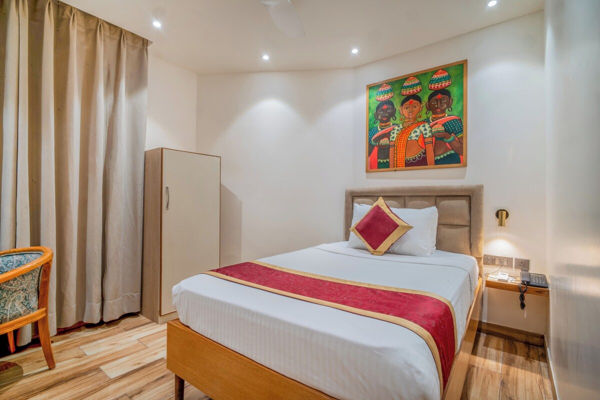 A hotel room with a bed, a nightstand, a wardrobe, a chair, and a painting on the wall.