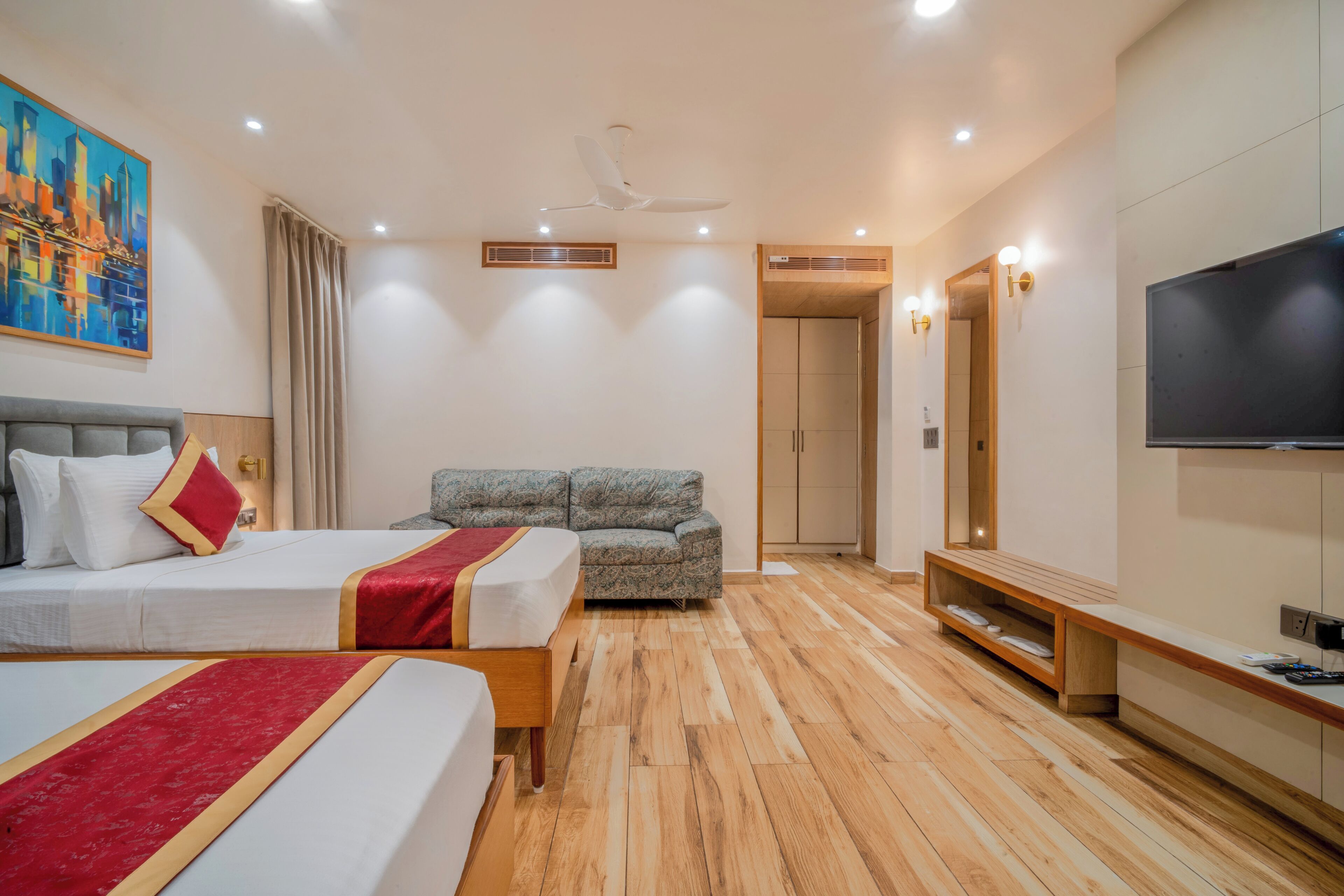 A hotel room with two beds, a sofa, a TV, and a painting on the wall.