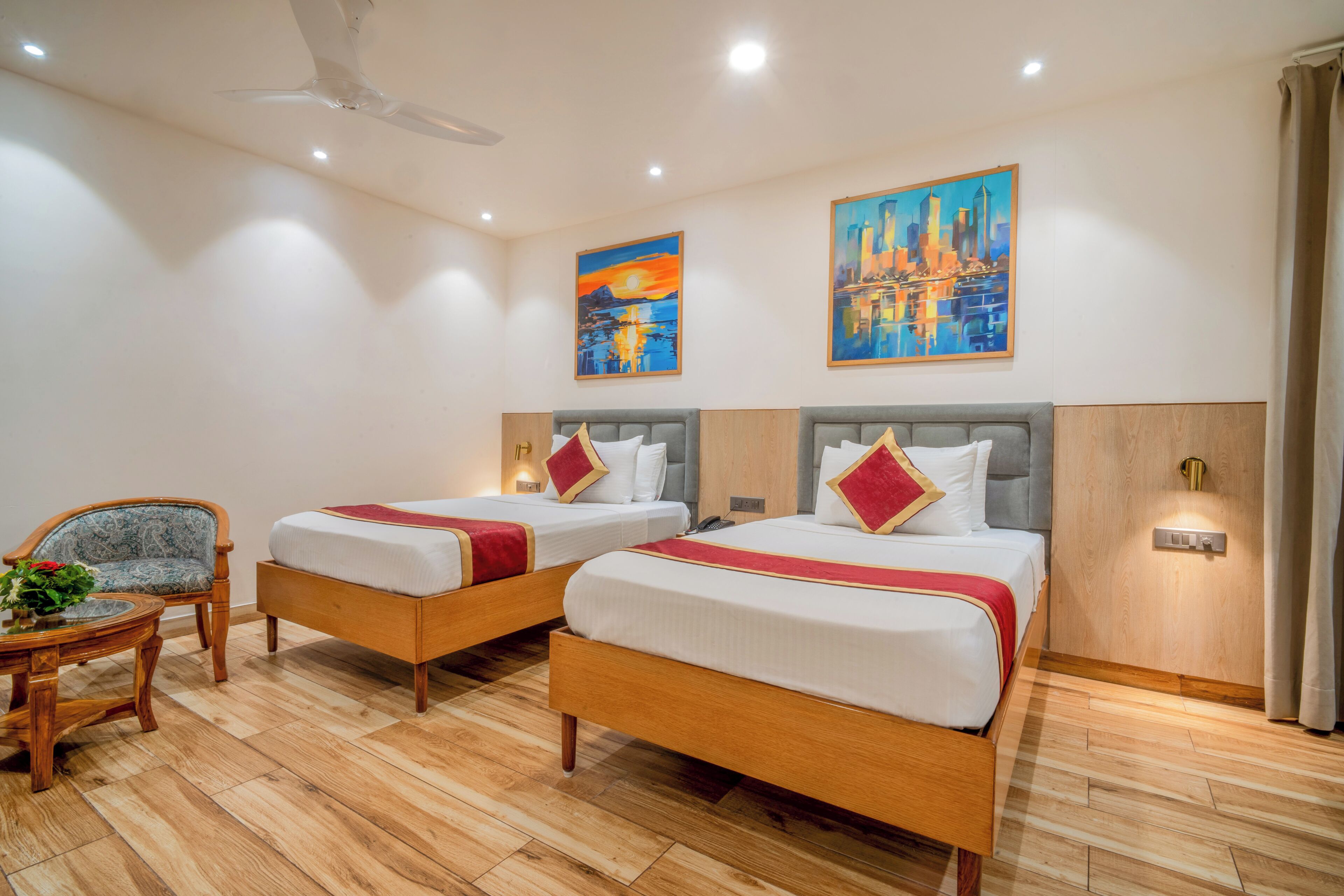 Een hotelkamer met twee bedden, een stoel, een tafel en kunstwerken aan de wanden.