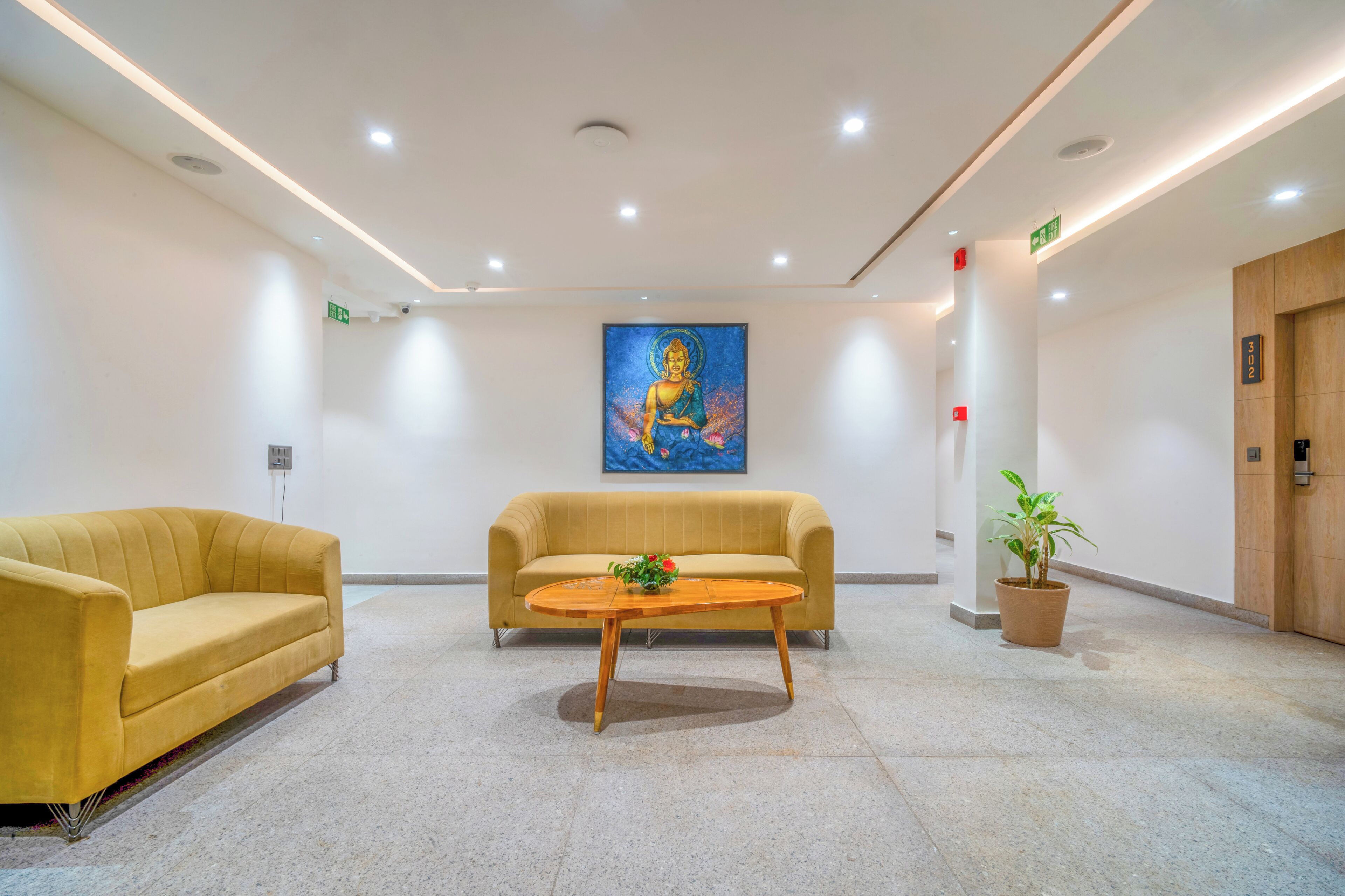 Eine Lobby mit einem gelben Sofa, einem Holztisch und einem Buddha-Gemälde an der Wand.