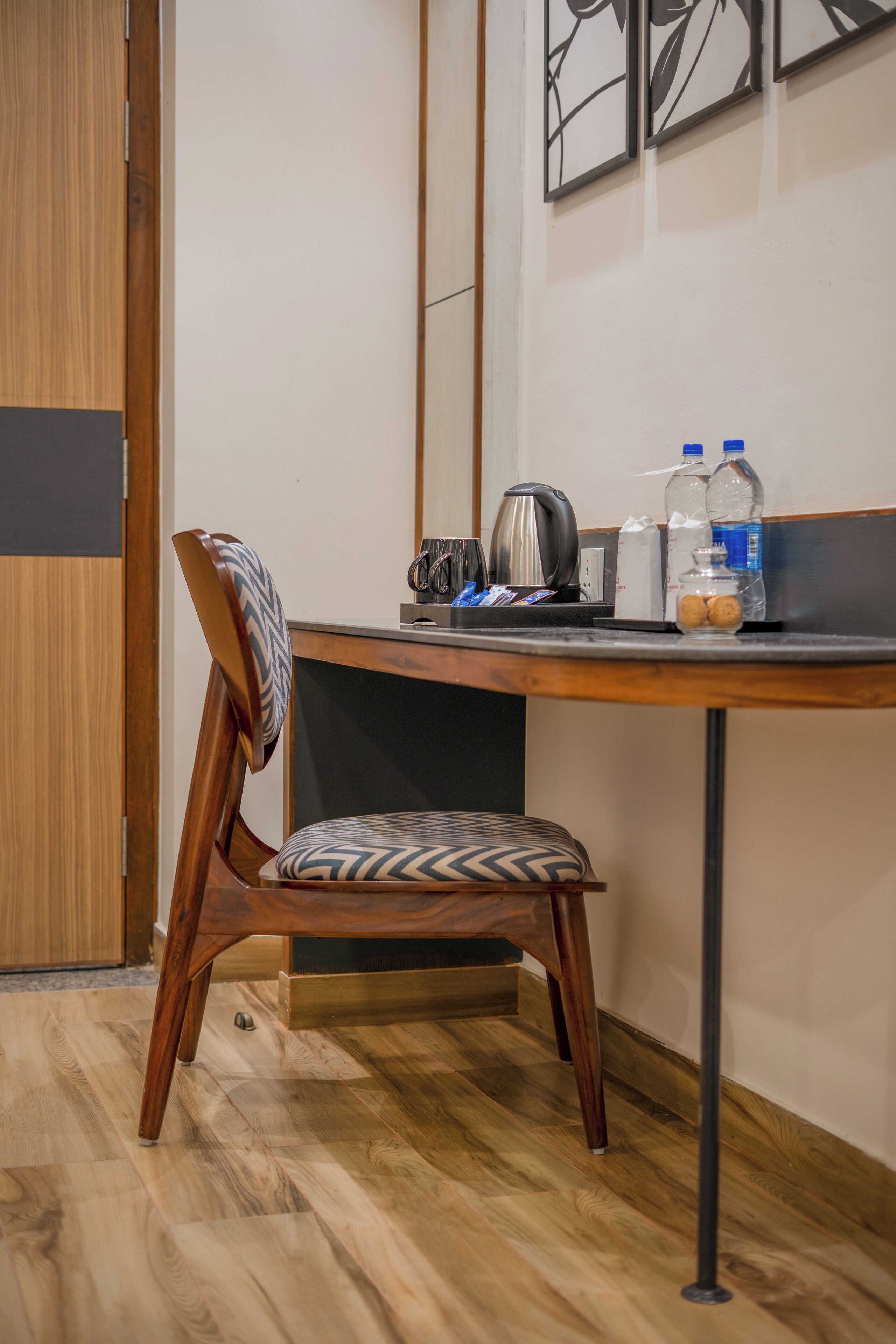 En træstol med et mønstret sæde, et træbord med sort overflade og en væg med indrammede kunstværker.
