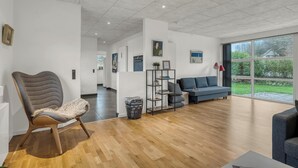 Un salon moderne avec un plancher en bois, un fauteuil recouvert d’un tissu gris, un canapé bleu et une étagère noire.