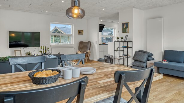 Un salon moderne avec une table à manger en bois, des chaises noires, un canapé gris et un téléviseur fixé au mur.