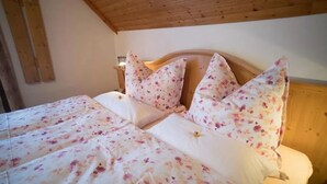 A bed with floral bedding and wooden headboard in a room with wooden ceiling beams.