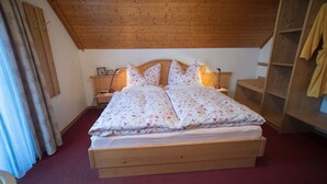 A wooden bed with floral bedding in a room with a sloped ceiling and wooden furniture.