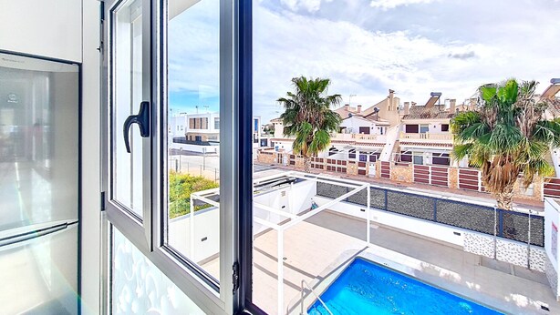 Blick von einem Balkon mit Swimmingpool, Palmen und einer Stadt im Hintergrund.
