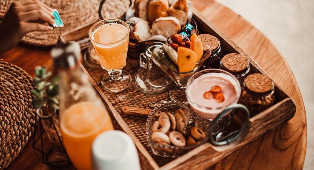 Un plateau en bois contenant divers aliments, notamment du pain, des noix et un verre de jus d’orange.