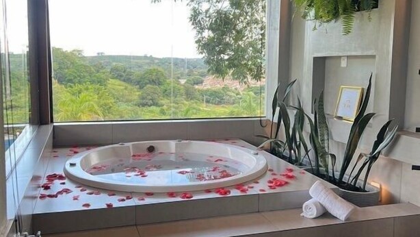 A spa area with a hot tub surrounded by rose petals, a wooden bench, and a view of greenery. - Chalé Village Jângal (Machado)