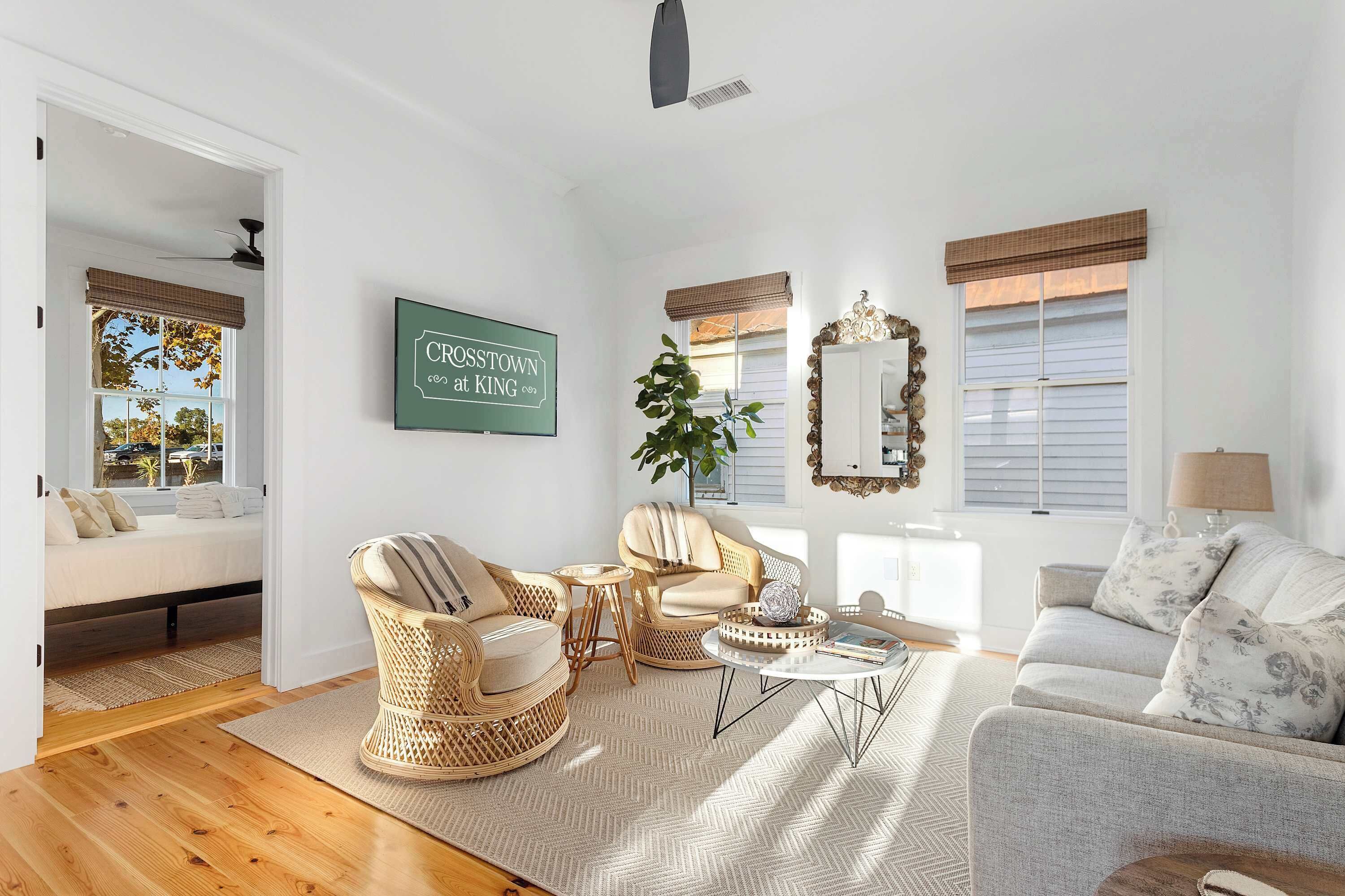A bright living room with a sofa, two armchairs, a coffee table, and a large mirror. A sign on the wall reads "CROSSTOWN at KING."