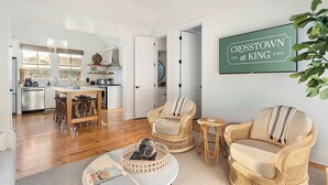 A spacious living area with a dining table, wicker chairs, and a coffee table. A sign on the wall reads "CROSSTOWN at KING." - Crosstown @ King | Downtown Dream - Walk to King! (Charleston)