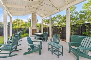 An outdoor patio with green chairs and a table, surrounded by a wooden fence and trees.