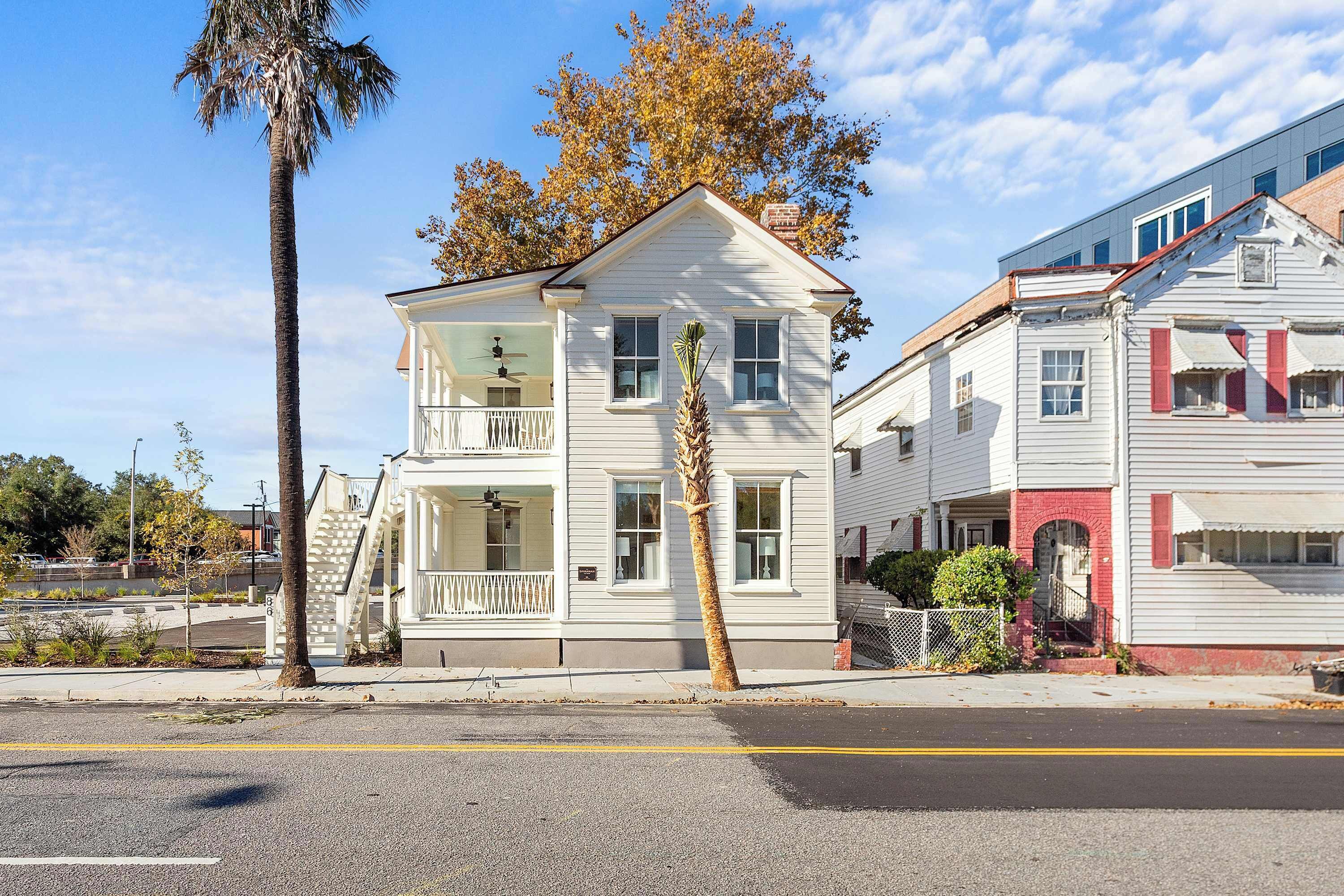 A two-story white house with a balcony, a palm tree, and a red brick section.