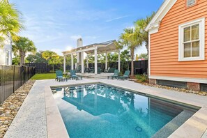 Ein Swimmingpool mit einer Pergola und Liegestühlen, umgeben von einem Zaun und Palmen.