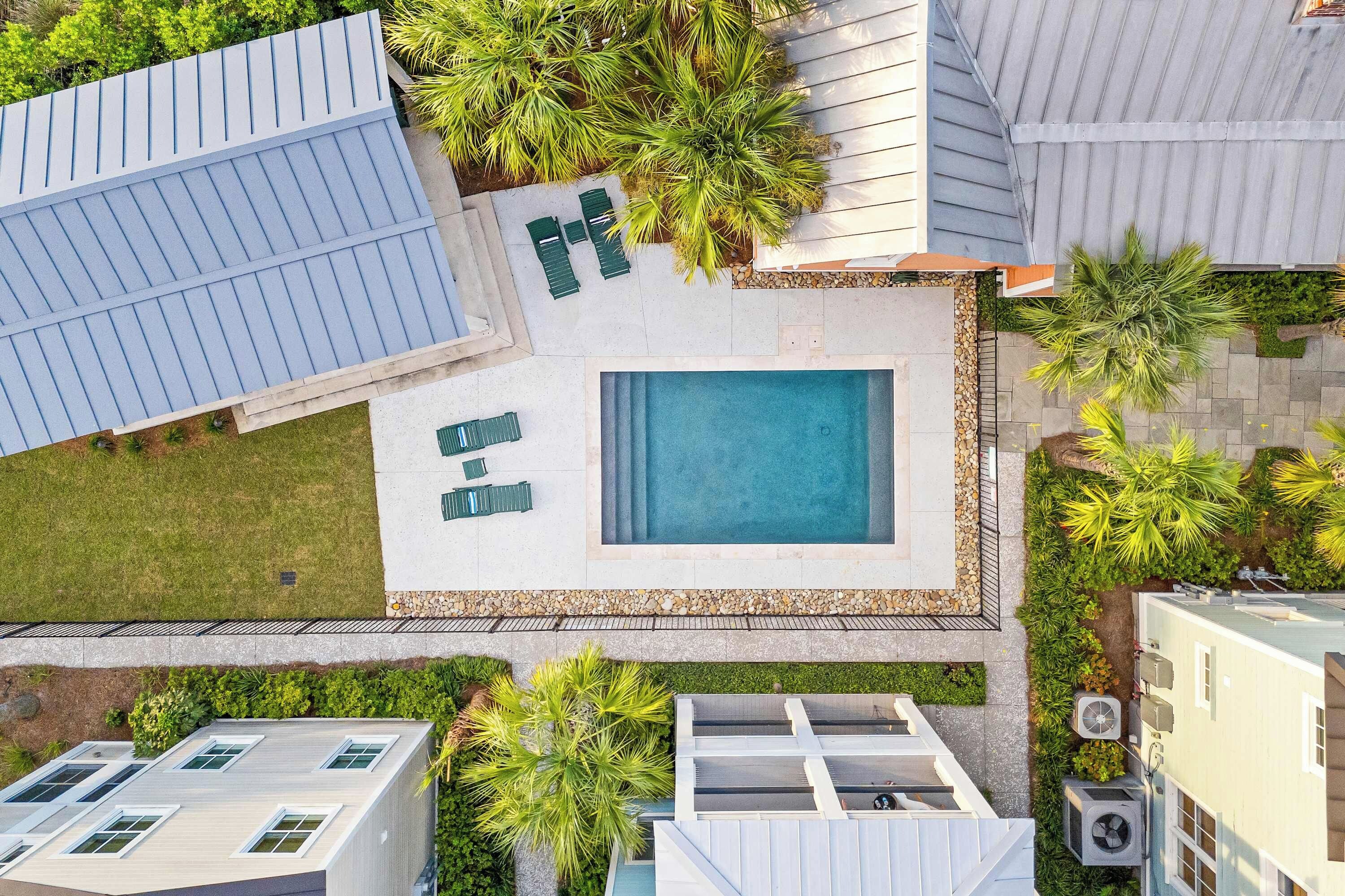 A residential area with a swimming pool, green outdoor furniture, and surrounding vegetation.
