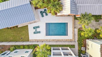 A residential area with a swimming pool, green outdoor furniture, and surrounding vegetation.