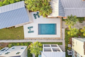 Zona residencial con piscina, mobiliario exterior verde y vegetación circundante.