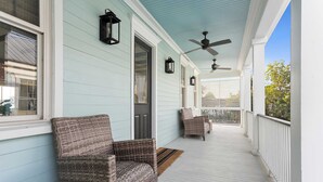 Eine überdachte Veranda mit Korbstühlen, Deckenventilator und einer Tür.