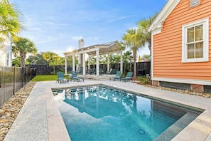 Ein Swimmingpool mit einer Pergola und Liegestühlen, umgeben von einem Zaun und Palmen.