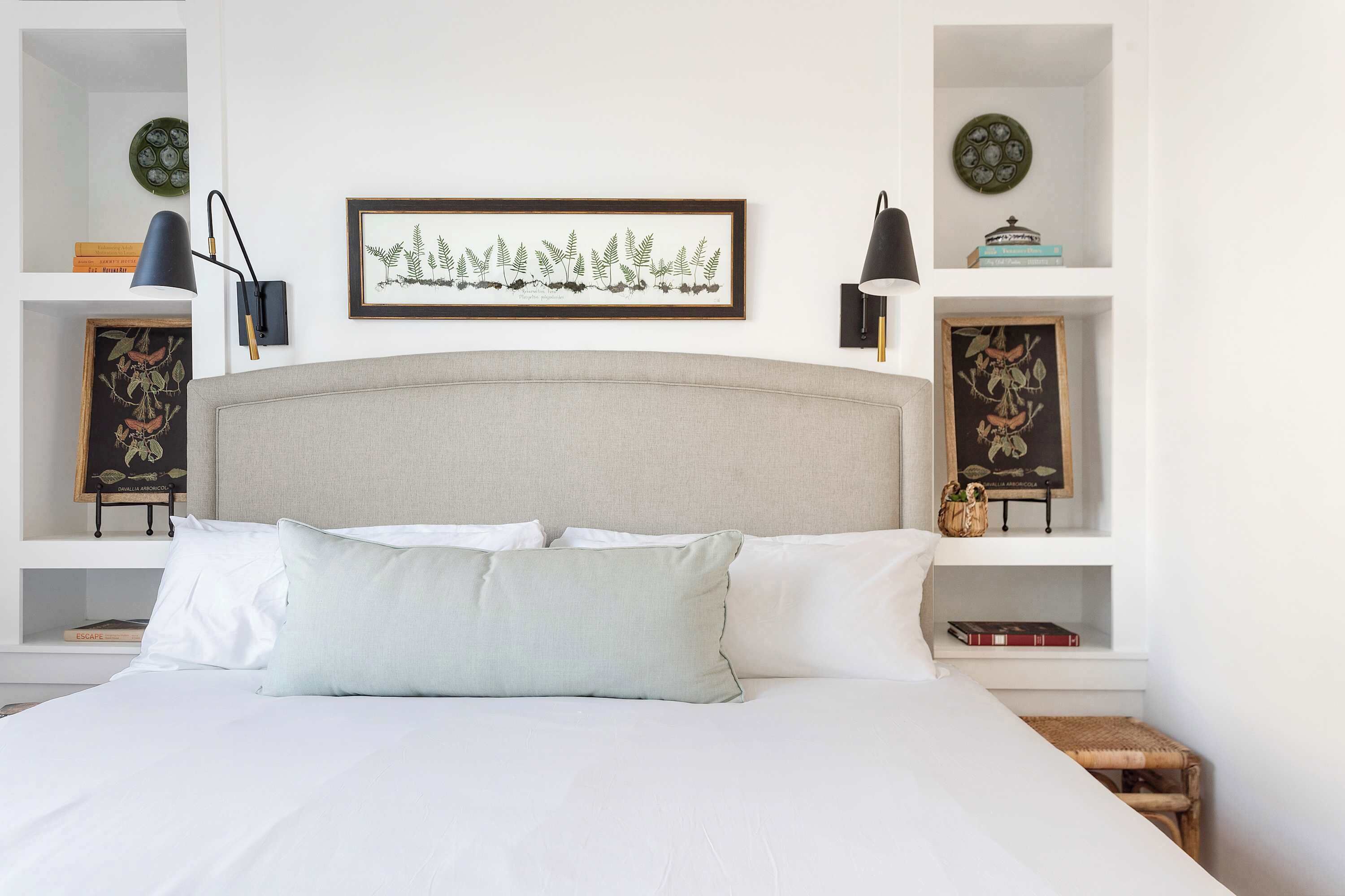 A neatly arranged bedroom with a large bed, two bedside tables with lamps, and wall-mounted shelves with decorative items.