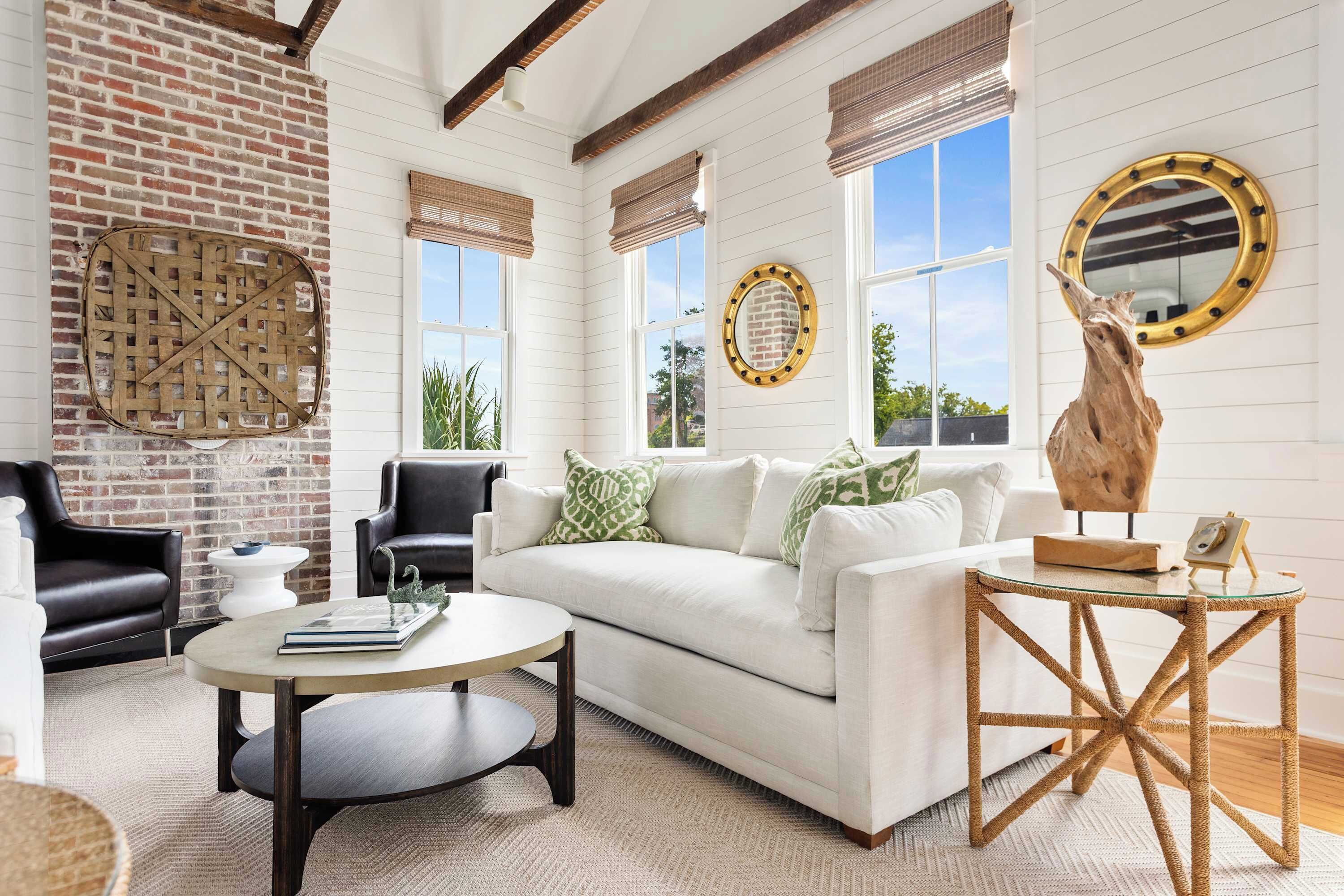 A cozy living room with a white sofa, black leather chairs, a round coffee table, and a rustic wooden side table.