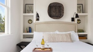 A neatly made bed with a tray of wine glasses and a bottle, a headboard, and shelves with books and decorative items. - Cozy 5BR/5BA Downtown Gem - Close to King! (Charleston)