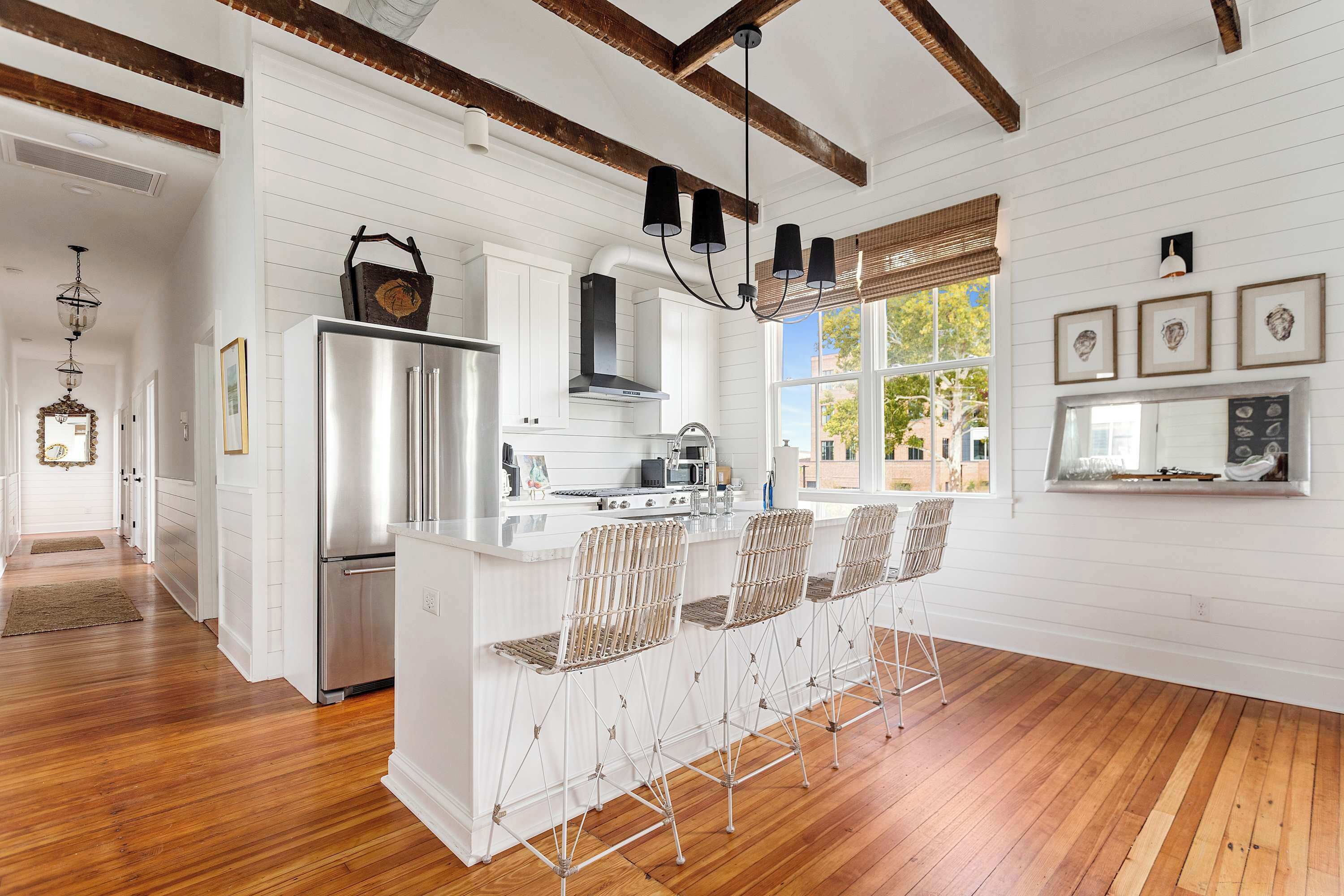 A kitchen with white cabinetry, a stainless steel refrigerator, a gas stove, and a bar area with metal stools.