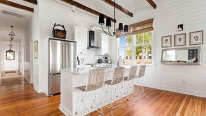 A kitchen with white cabinetry, a stainless steel refrigerator, a gas stove, and a bar area with metal stools. - Cozy 5BR/5BA Downtown Gem - Close to King! (Charleston)