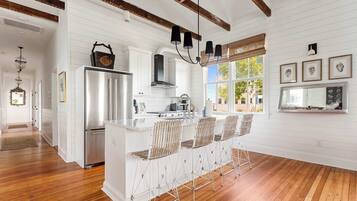 A kitchen with white cabinetry, a stainless steel refrigerator, a gas stove, and a bar area with metal stools.