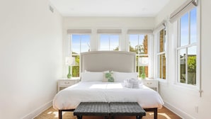 A spacious bedroom with a large bed, two bedside tables, a bench, and a view of the outdoors through large windows.