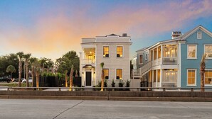 A row of coastal-style houses with balconies, a paved street, and palm trees. - Downtown 3BR Home - Near King Street! (Charleston)
