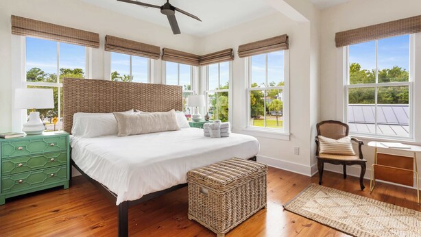 A bedroom with a large bed, a ceiling fan, and a view of the outdoors through large windows. - Downtown 3BR Home - Near King Street! (Charleston)