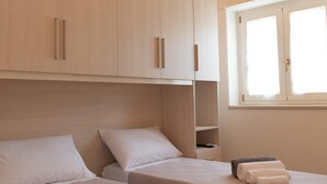Una habitación con dos camas, armarios de madera, un ventanal y una lámpara en el techo.