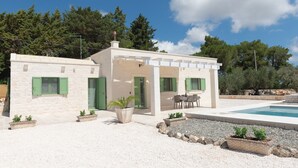 Una casa de dos pisos con piscina, mobiliario exterior y un jardín.