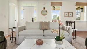 Una sala de estar con un sofá color crema, un espejo redondo y una planta en maceta.