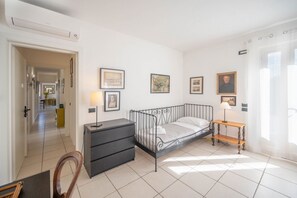 A bedroom with a metal bed frame, a bedside table with a lamp, a dresser, and framed pictures on the wall.