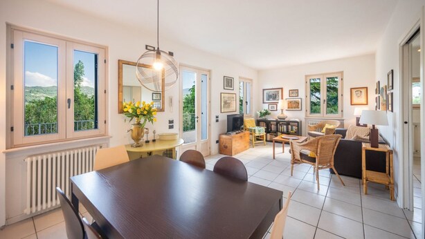 A spacious living area with a dining table, chairs, a sofa, and a television. - ApartmentsGarda - Ca' Capre 1 (GARDA)