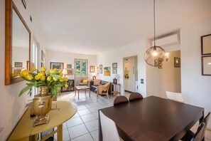 A modern living room with a dining table, sofas, and a coffee table. There are framed pictures on the walls and a vase with flowers on the coffee table.