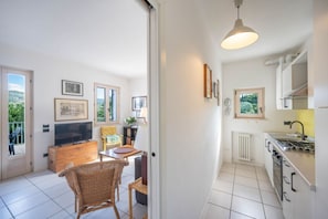 A modern kitchen with white cabinets, a stove, and a dining area with a wicker chair and table.