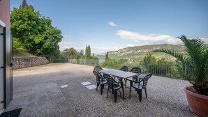 An outdoor patio with a table and chairs, a stone wall, and a view of a lake and hills. - ApartmentsGarda - Ca' Capre 1 (GARDA)