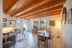A spacious room with a wooden ceiling, a dining table with chairs, a sofa, a TV, and framed pictures on the walls.