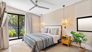 A bedroom with a bed, bedside tables, a ceiling fan, a large window, and a potted plant. - Brand New Tropical Oasis Expansive Outdoor Space (Playa Langosta)