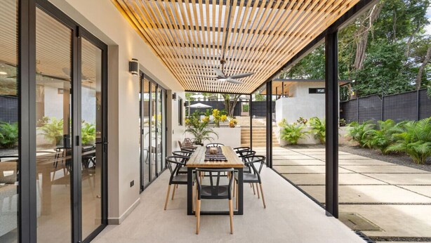 A covered patio area with a dining table and chairs, surrounded by glass doors and a view of the garden. - Brand New Tropical Oasis Expansive Outdoor Space (Playa Langosta)