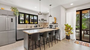 A modern kitchen with a central island, bar stools, a refrigerator, and a dining area with a view. - Brand New Tropical Oasis Expansive Outdoor Space (Playa Langosta)