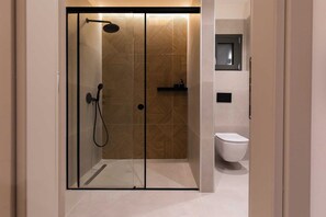 Ein modernes Badezimmer mit einer Duschkabine, einer Toilette und einem kleinen Ablagebereich für Pflegeprodukte.